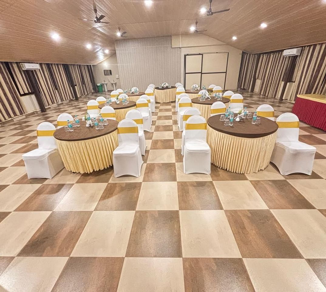 A banquet hall with round tables and chairs set for an event, featuring a checkered floor and soft lighting | Ballroom | Woodstock Resorts, Coorg