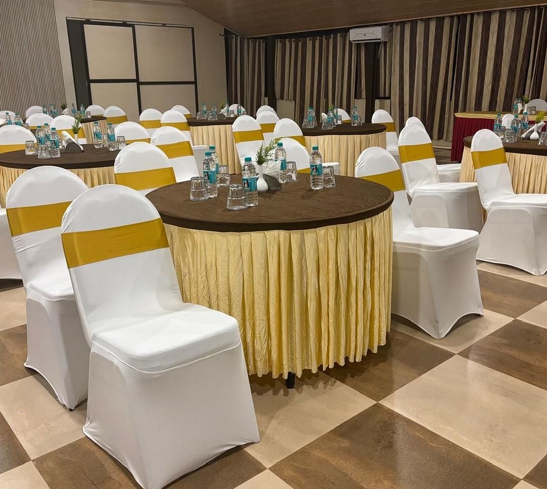 A closer view focuses on one of the round tables in the banquet hall, adorned with floral centrepieces and surrounded by chairs with white covers | Ballroom | Woodstock Resorts, Coorg