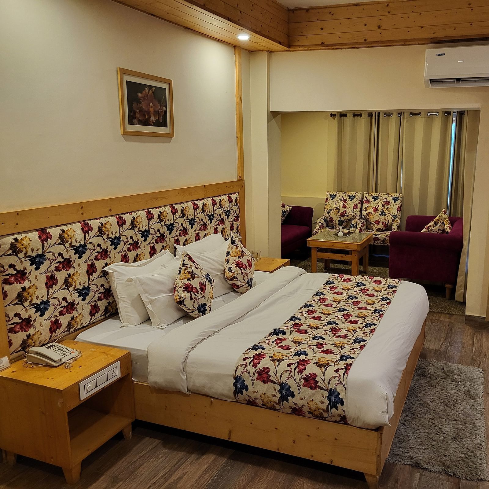 A bedroom setup with wooden accents, floral cushions, and a seating space by the window at Dagshai Manor Kasauli - Inde Hotels.
