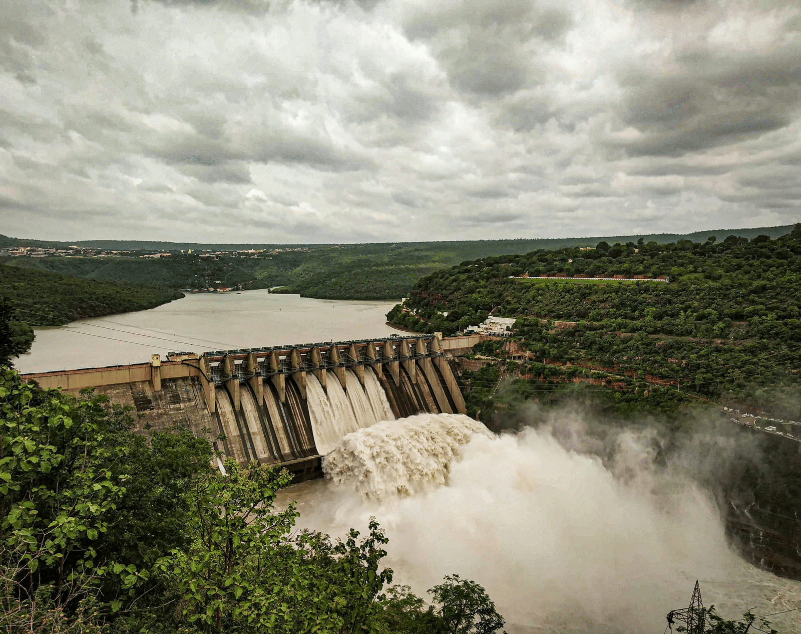A large dam with water flowing through its gates into a wide river under a cloudy sky.