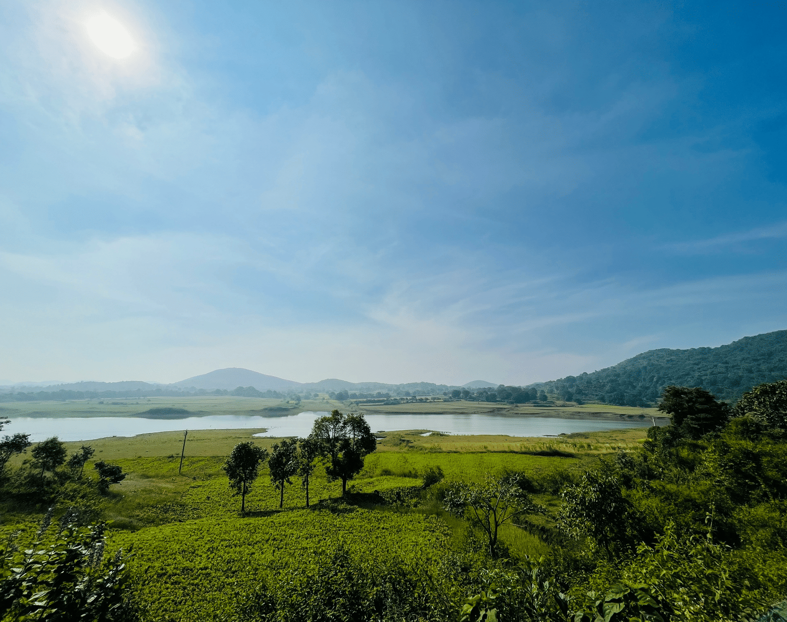 Scenic view of a lush green landscape with a river and hills under a bright blue sky.
