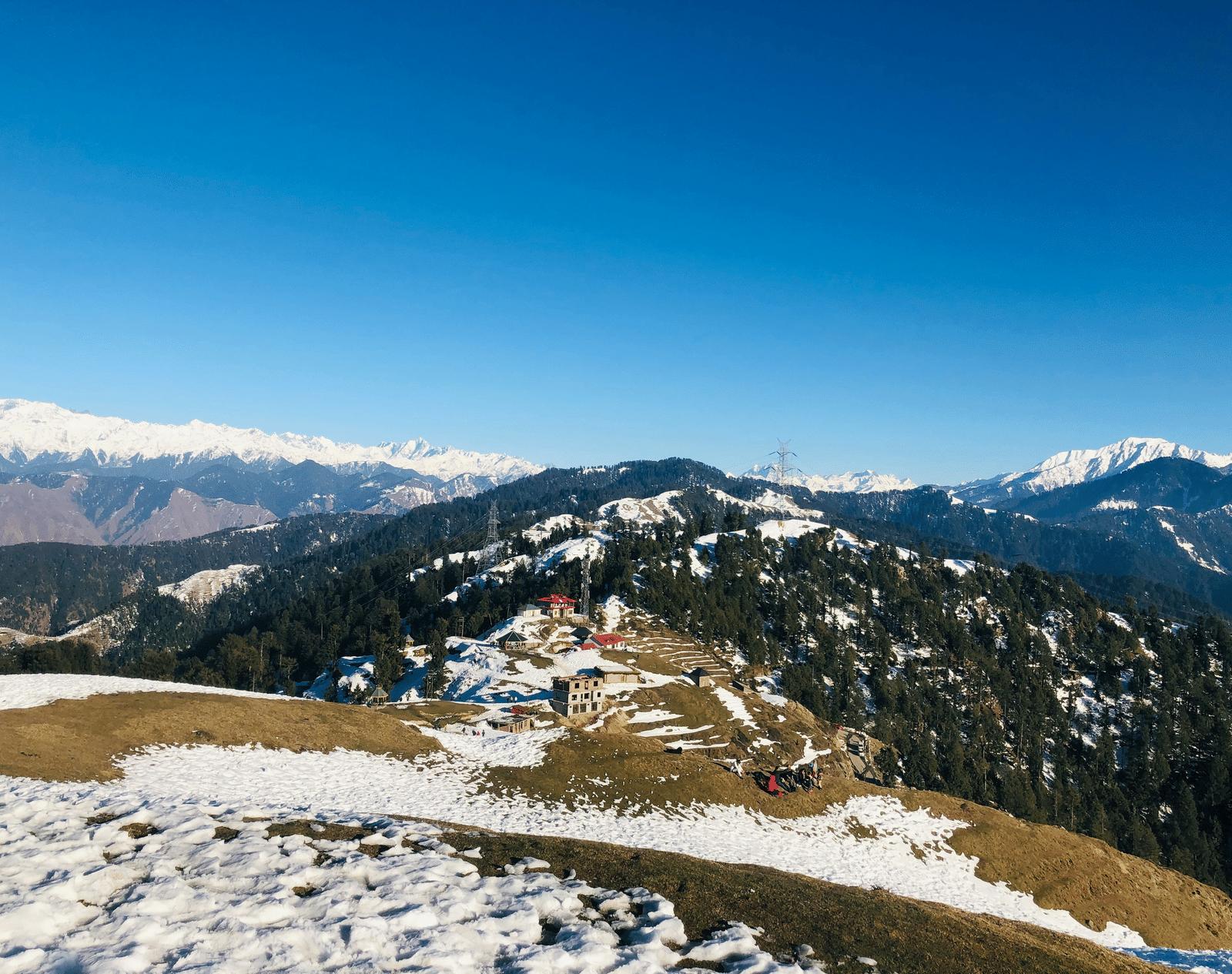 A snow-covered mountain slope with patches of green grass under a clear blue sky.