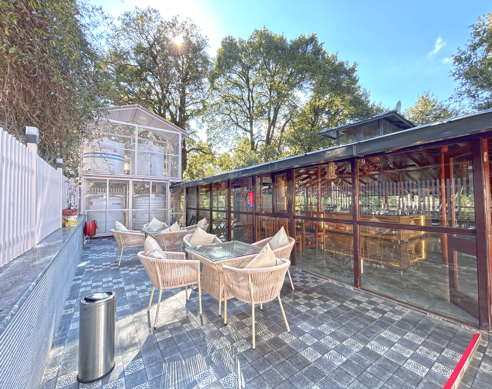 The exterior image of the restaurant featuring chairs and tables with the background of a clear sky and trees - DLS The Emerald, Nainital