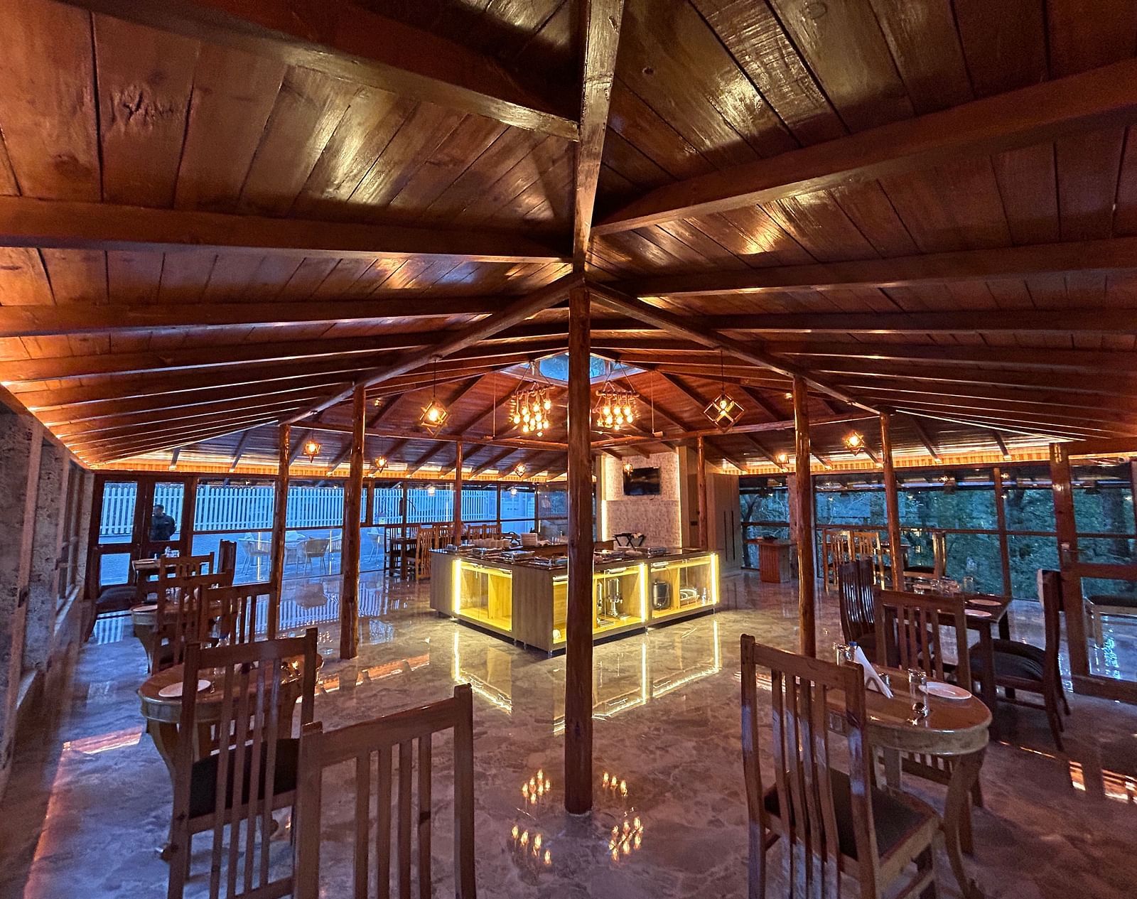 An image of the restaurant at DLS The Emerald, Nainital with wooden interiors along with chairs and tables and the area is lit with bright lighting