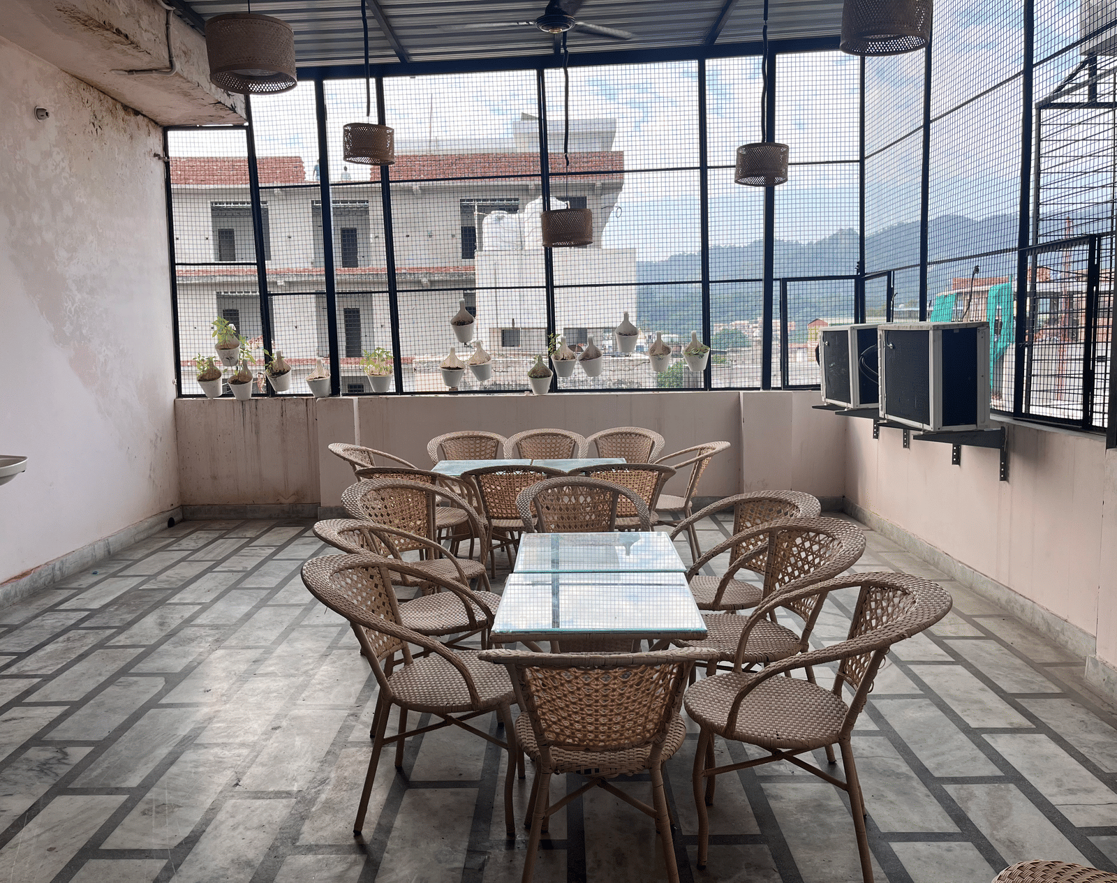 2 dining tables featuring a glass surface lined with bamboo chairs on the rooftop dining area at Perfectstayz Value Dhruv Nanda, Haridwar.