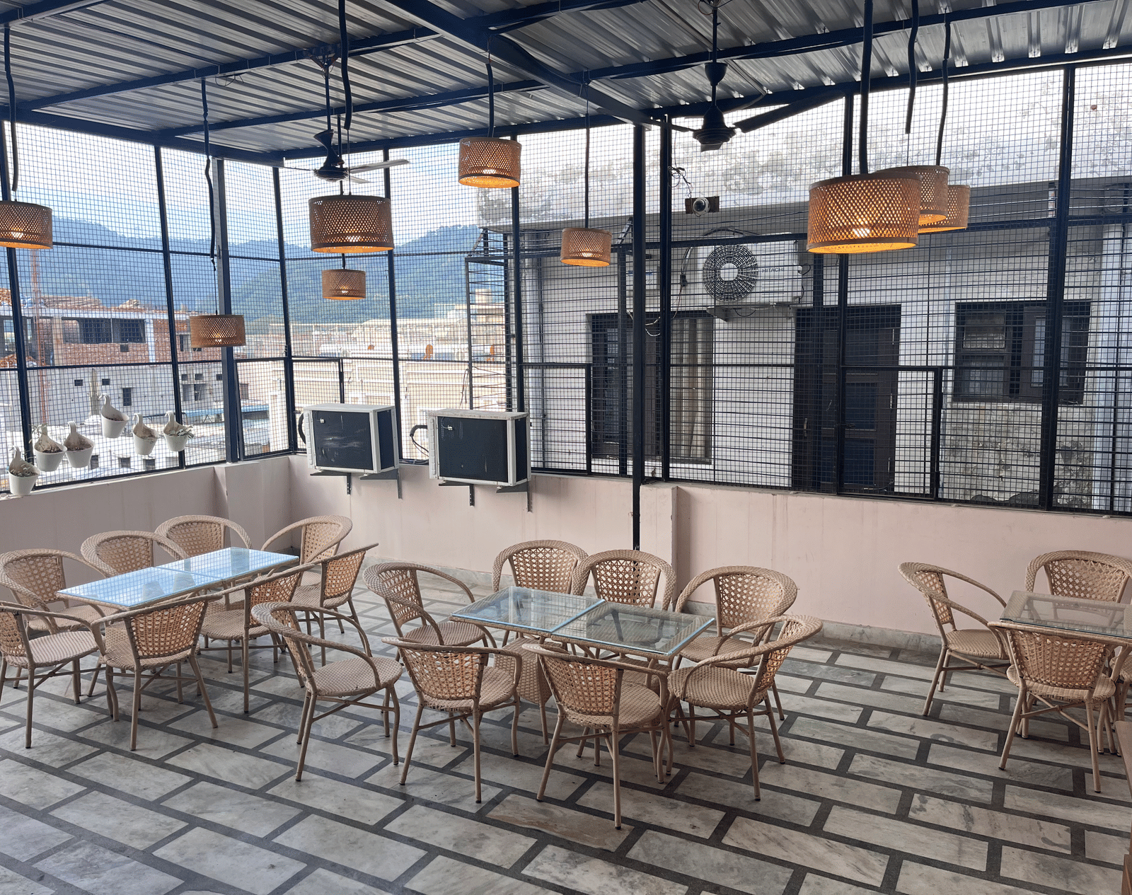 Full view of the rooftop restaurant at Perfectstayz Value Dhruv Nanda, Haridwar, with warm lights hanging from the tin ceiling along with a beautiful mountains in the background.