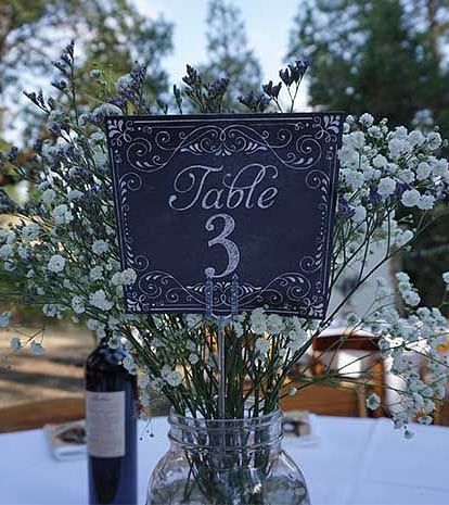 A board which says table 3 placed on a table alongside a bottle of wine - Shaver Lake Village Hotel.