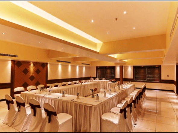 Banquet hall with arranged tables and chairs, ceiling lights, and wooden wall panels.