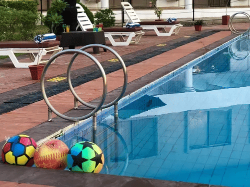 A swimming pool at the VITS Kamats Resort, Silvassa, with poolside chairs and colourful balls placed on the edge. gas68q
