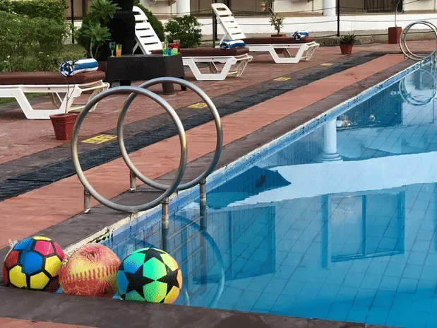 A swimming pool at the VITS Kamats Resort, Silvassa, with poolside chairs and colourful balls placed on the edge. gas68q