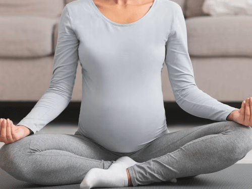 A pregnant woman sitting in a yoga pose, practicing prenatal yoga in a cozy living room.