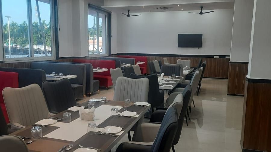 A dining area is set with tables, chairs with red and grey upholstery, and large windows - Kankidham Lords Inn