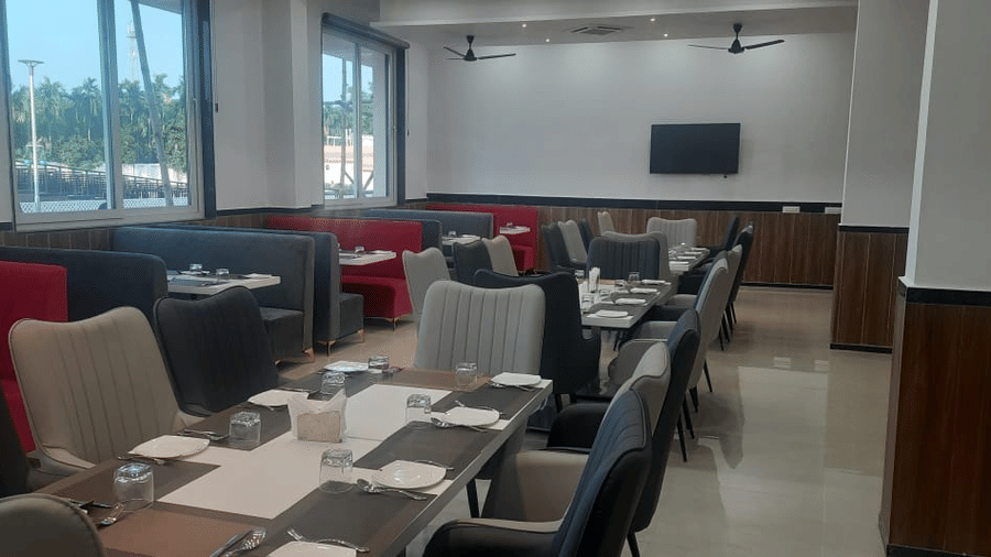A dining area is set with tables, chairs with red and grey upholstery, and large windows - Kankidham Lords Inn
