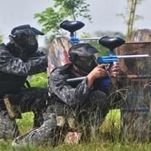 Several people in protective gear engaged in a paintball game in an outdoor setting