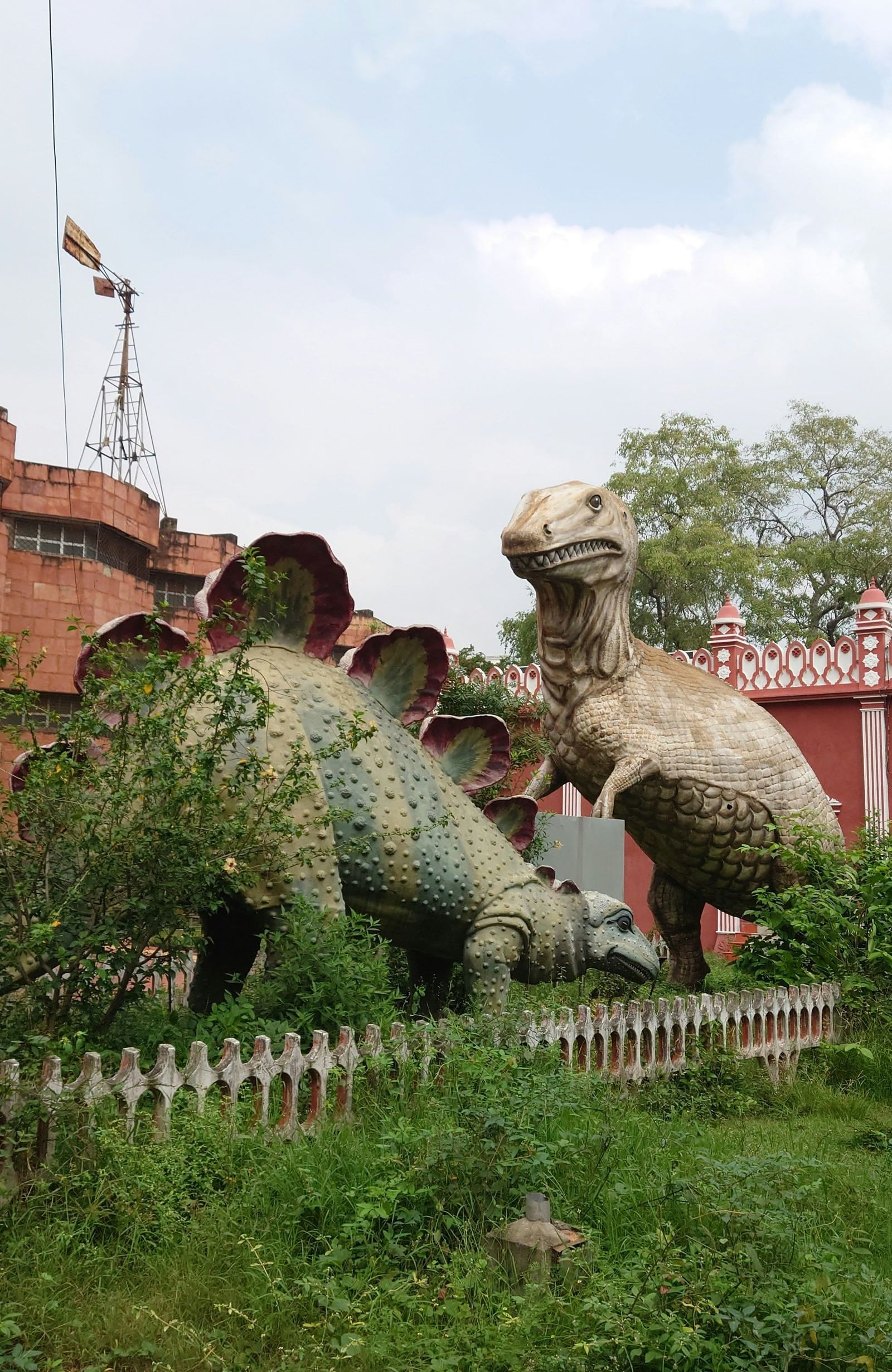 An image of a museum featuring two statues of dinosaurs  and behind there is a building  