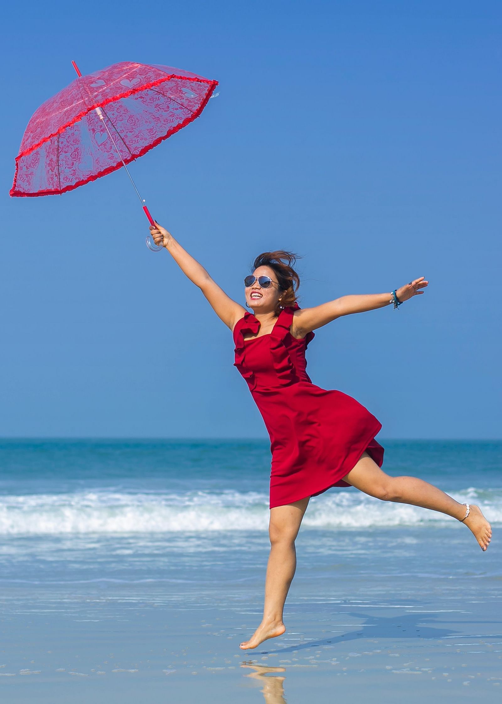a woman jumping while holding an umbrella on the beach - Caravela Beach Resort Goa