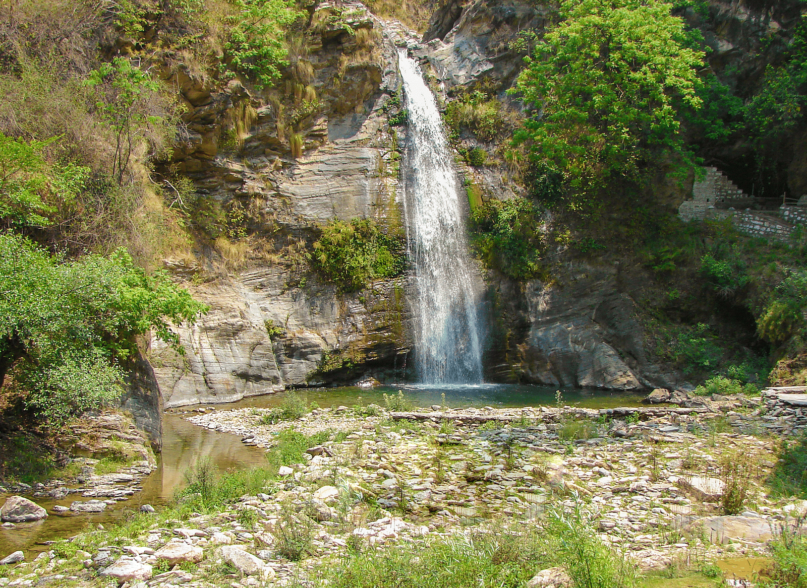 A view of the waterfall cascading on a puddle of water during daylight.