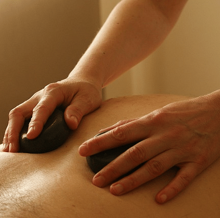 Two hands of a masseuse with massage equipment cupped with their hand, orchestrating the procedure on the clients back