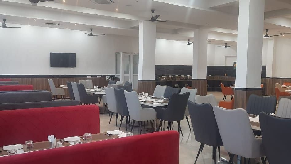 A brightly lit dining area features tables with red bench seating and grey chairs - Kankidham Lords Inn