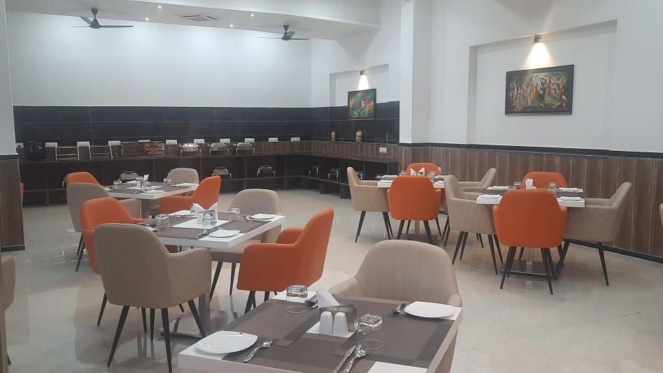 A dining area is set with round tables and orange chairs, with a long table against the wall - Kankidham Lords Inn