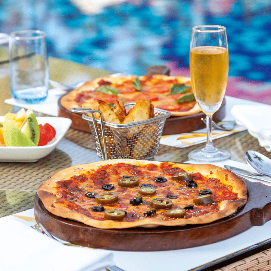 a pizza on a wooden plate kept on the table - Caravela Beach Resort Goa