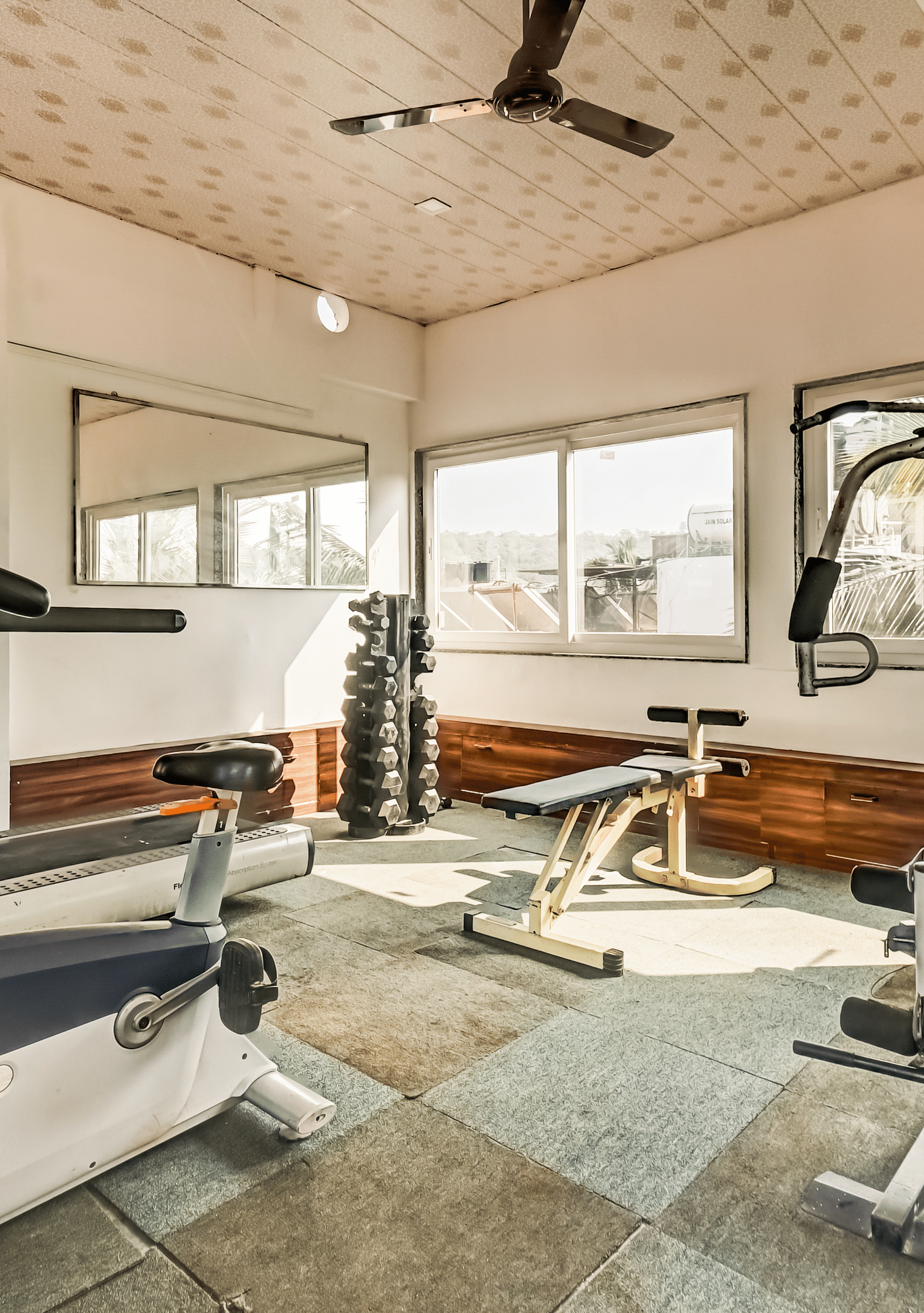  A gym with equipment neatly arranged and maintained, featuring large windows that flood the room with natural light