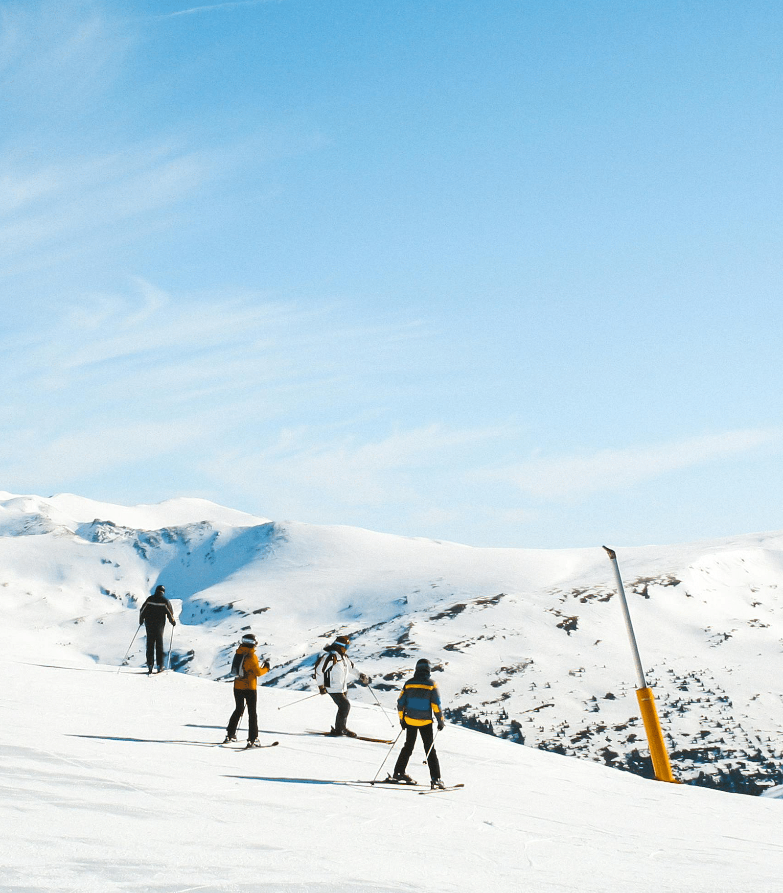 people scattered around warmly dressed with their skiing gears on a snowy plain with mountains in the background