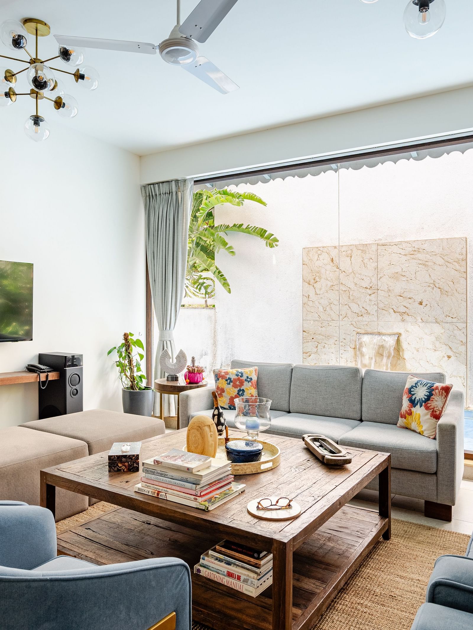 Modern living room with cosy sofas, a rustic wooden coffee table, wall-mounted TV, and large glass doors opening to a private water feature - Lindsay Manor