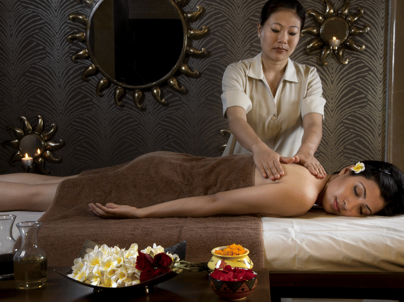 A guest lying on a spa bed receiving a massage from a therapist at Heritage Village Resorts & Spa, Manesar.