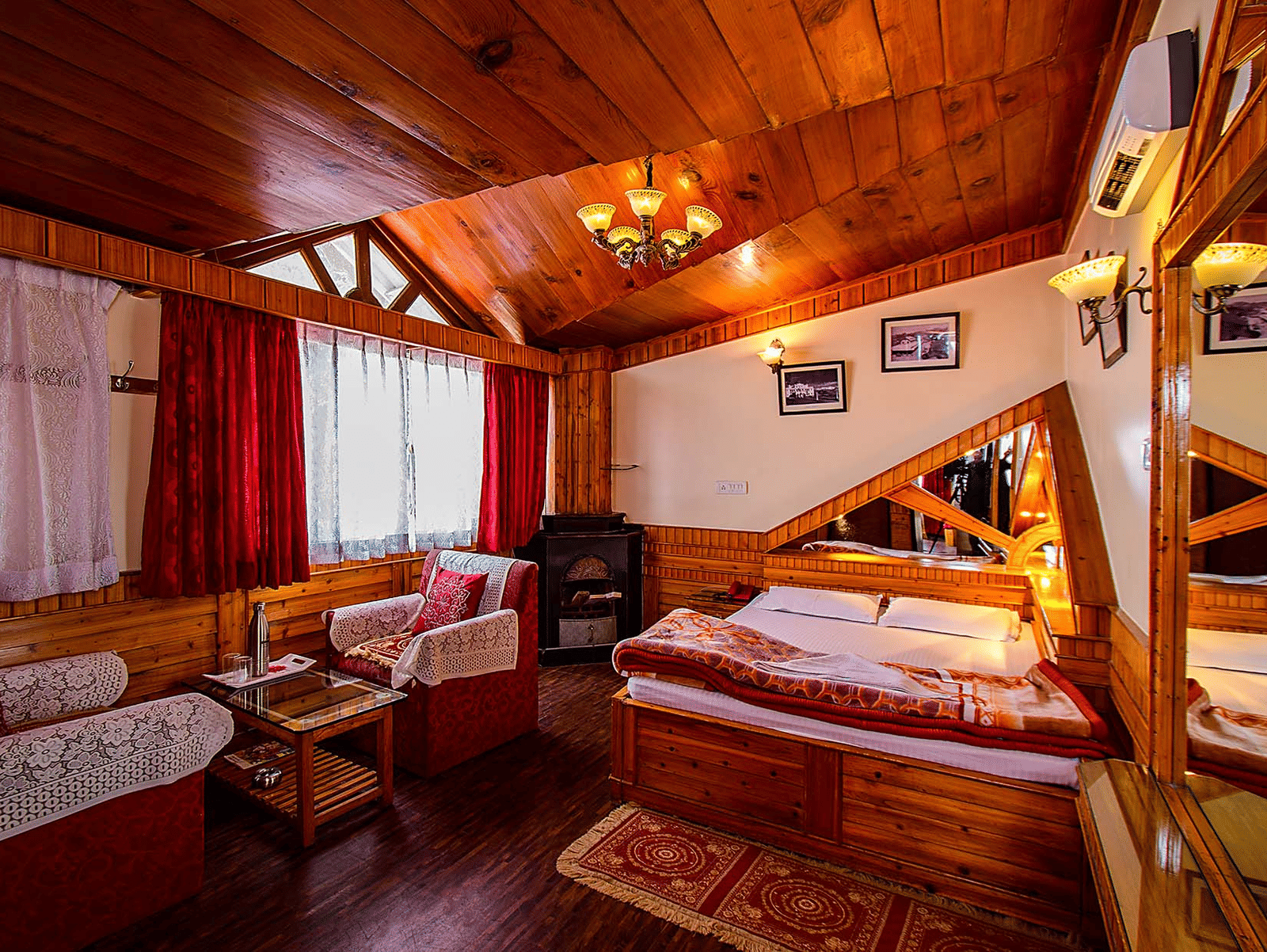 Hotel room with a wooden ceiling, double bed, red and white seating area, and wall mirrors reflecting the room at Hotel Dolphin Darjeeling.