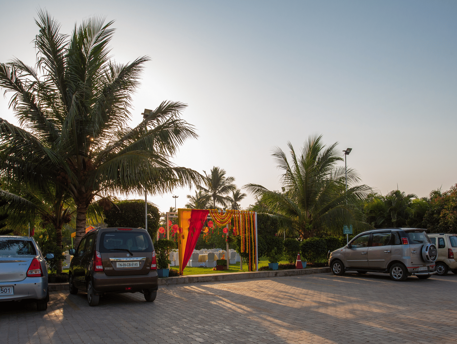 An outdoor parking area at our resort, with several cars parked under palm trees - Grande Bay Resort & Spa, Mamallapuram