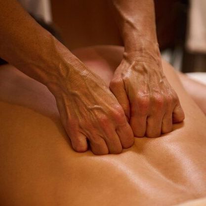 A spa therapist is giving a deep tissue back massage to a person lying face down, using their knuckles.