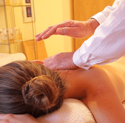 A person is receiving a massage on a spa table. The therapist's hands are gently massaging the person's back.