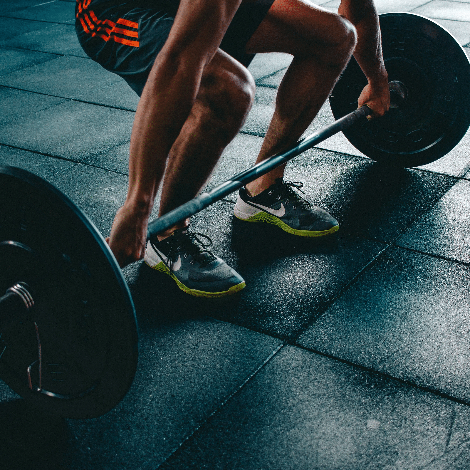 A person in athletic wear preparing to lift a barbell at a gym, captured mid-squat on a rubberised workout floor