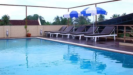 A swimming pool with a bunch of beach beads and two beach umbrellas near by, pictured during the day.