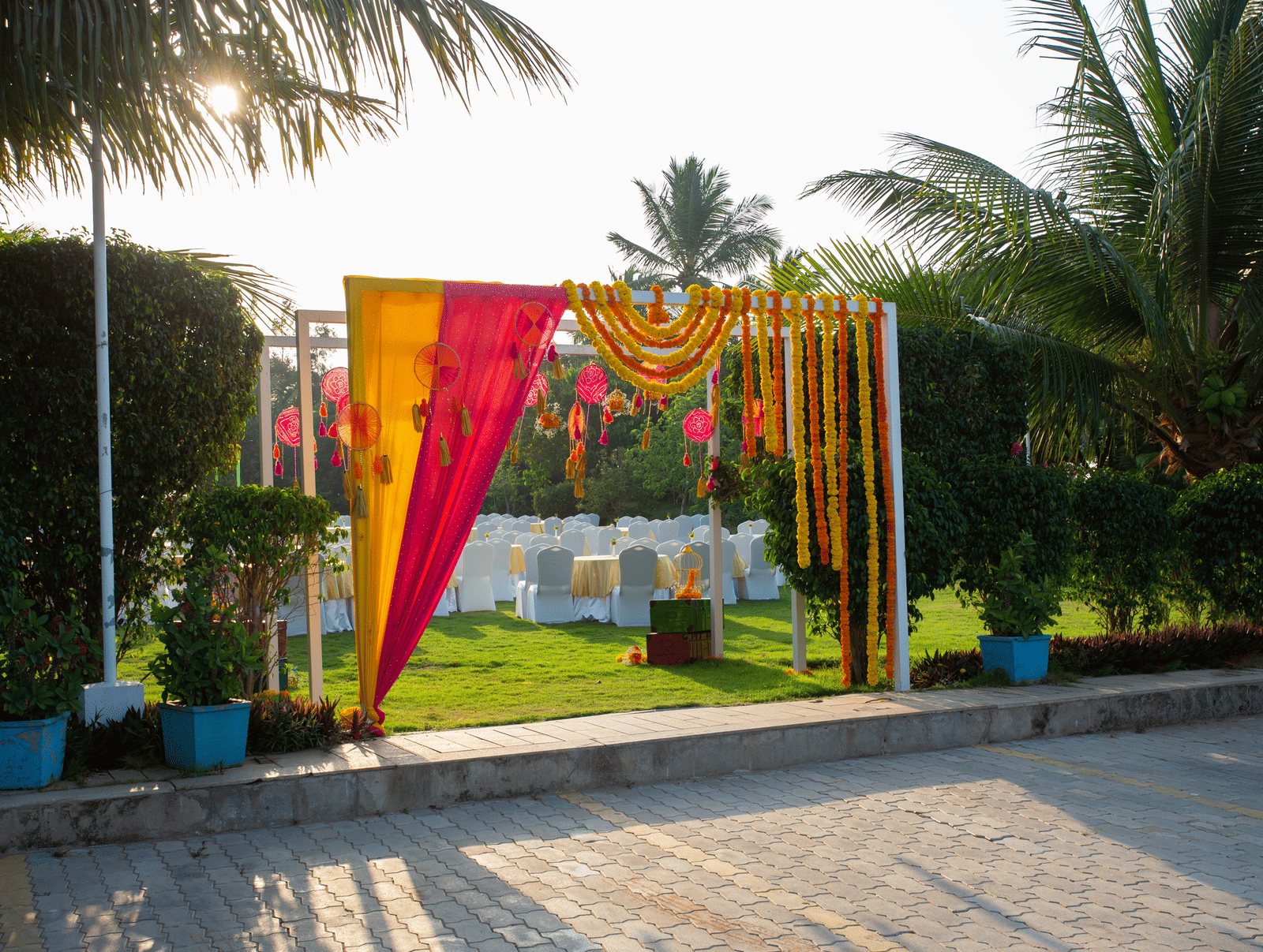 An outdoor event entrance decorated with pink and yellow fabric and marigold garlands, set on a paved area with palm trees - Grande Bay Resort & Spa, Mamallapuram