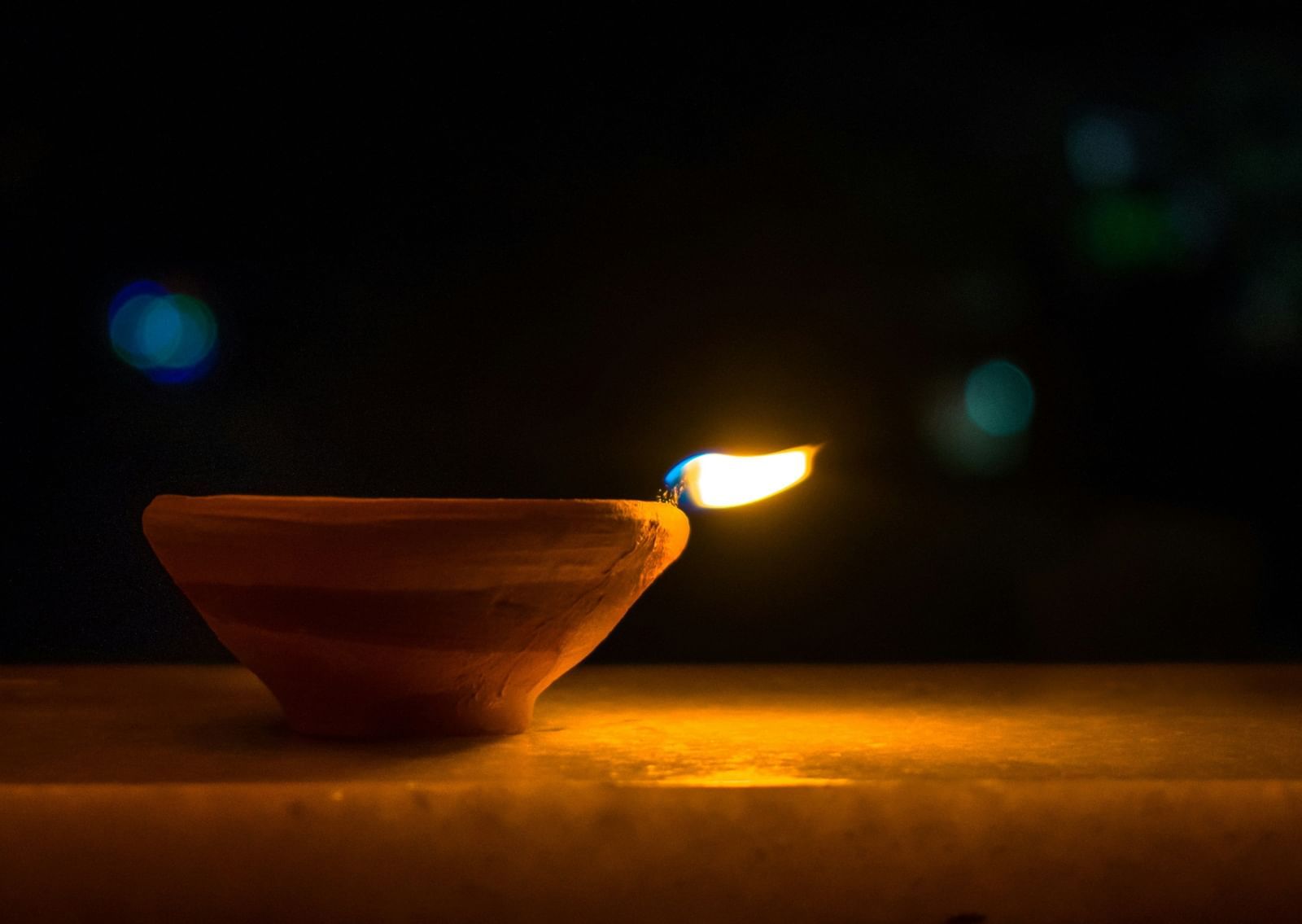 A close up of a lit diya that is placed on a marble with the background blurred.