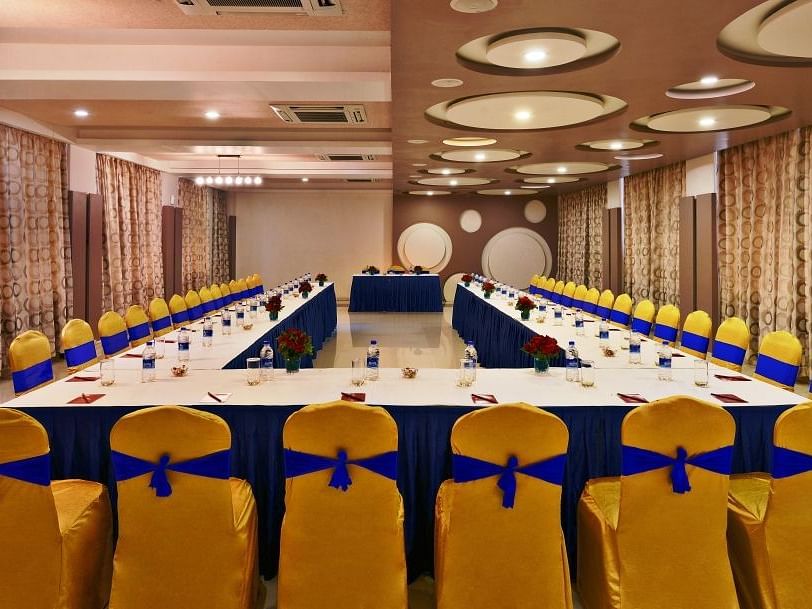 A formal meeting room setup at Lords Inn Porbandar, with a U-shaped table and chairs adorned with blue and yellow sashes.