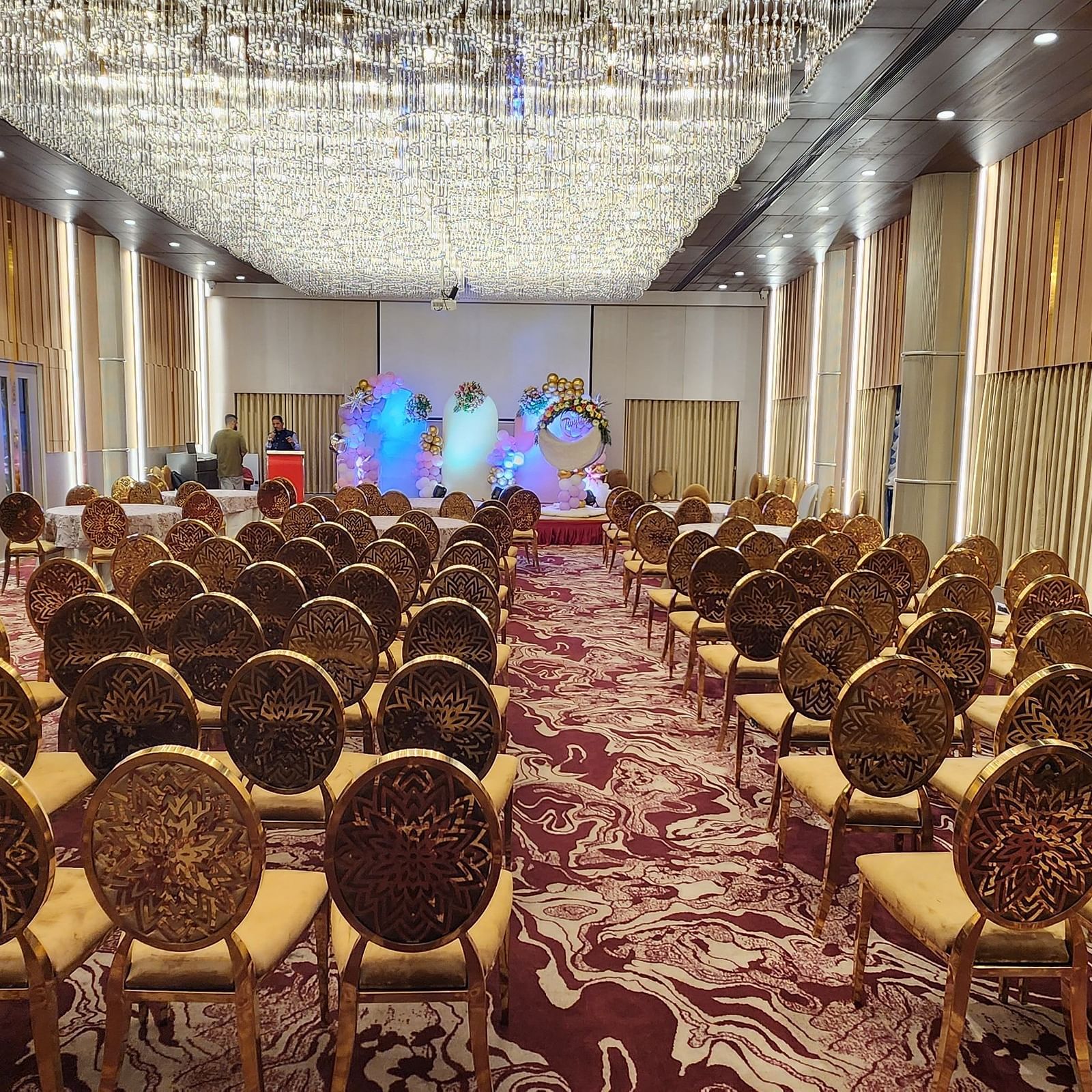 a banquet hall at Lords Inn Rajkot with theatre style seating arrangement with a buffet counter on side and a small stage area decorated at the front