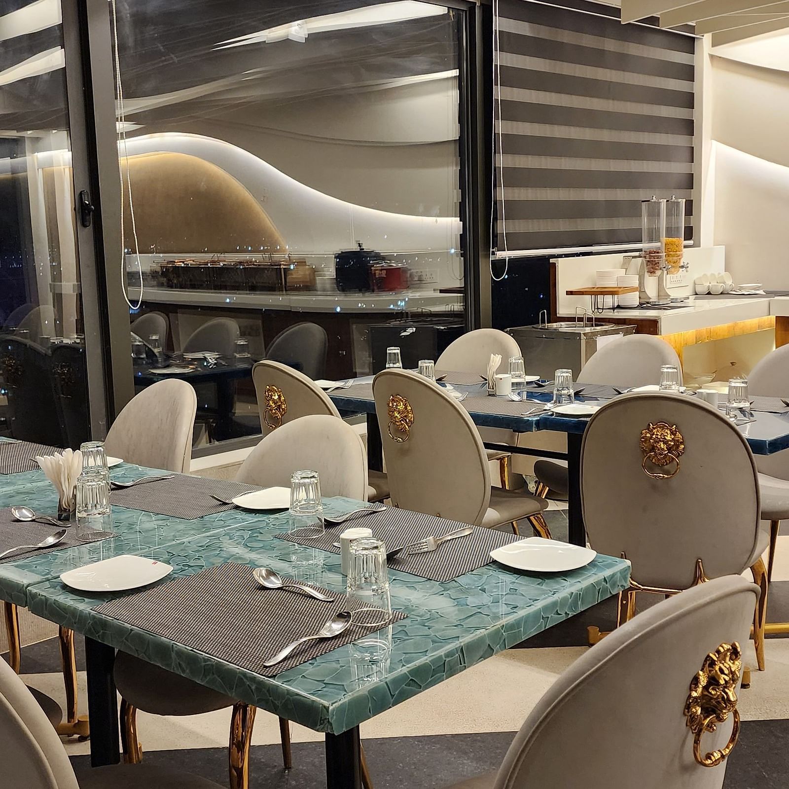 An elegant dining area with white and gold chairs and set tables, located beside large windows offering an outside view at Lords Inn Rajkot