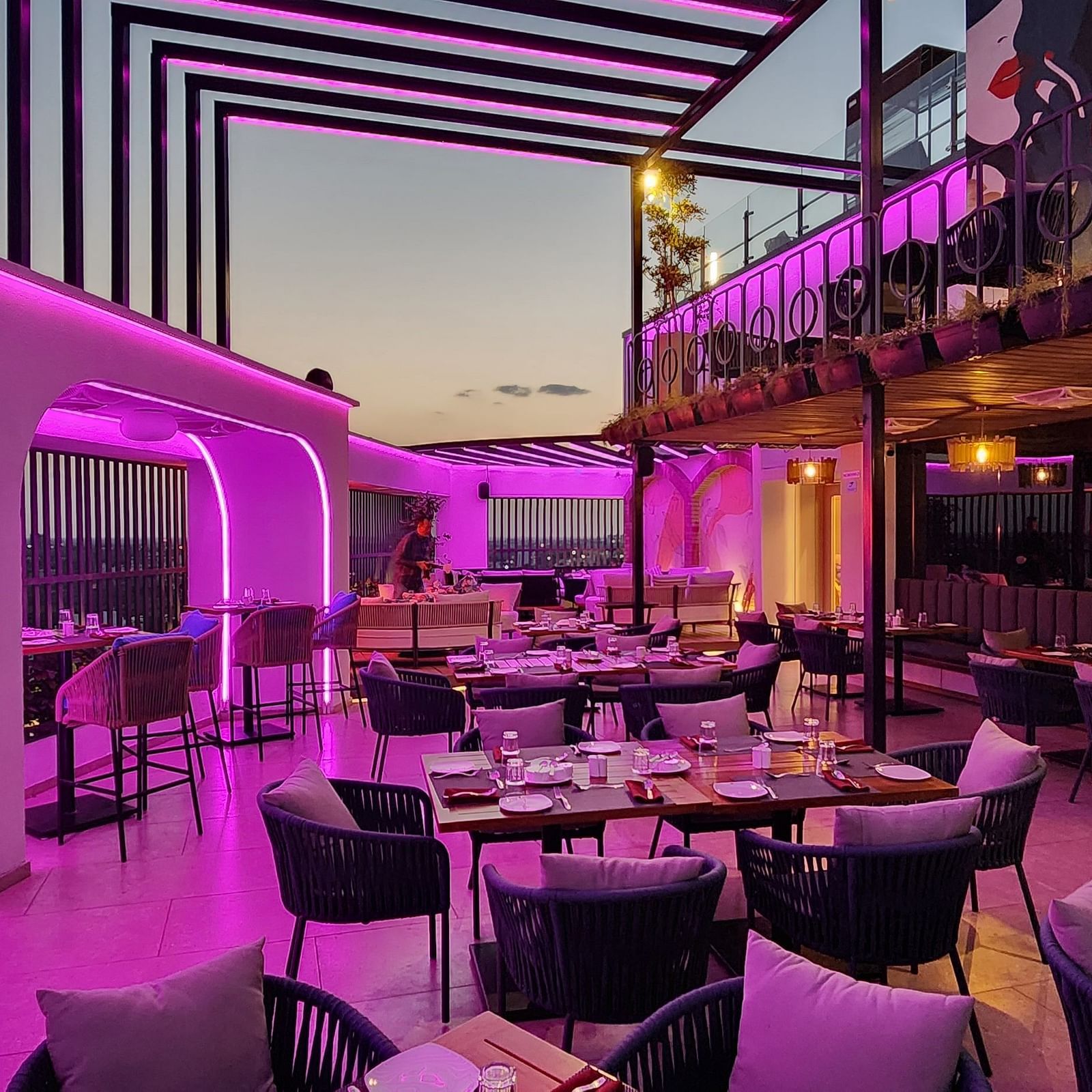 a rooftop dining area at Lords Inn Rajkot with variously arranged dining area on the floor, a balcony with seating area, and  a dimly lit ambience
