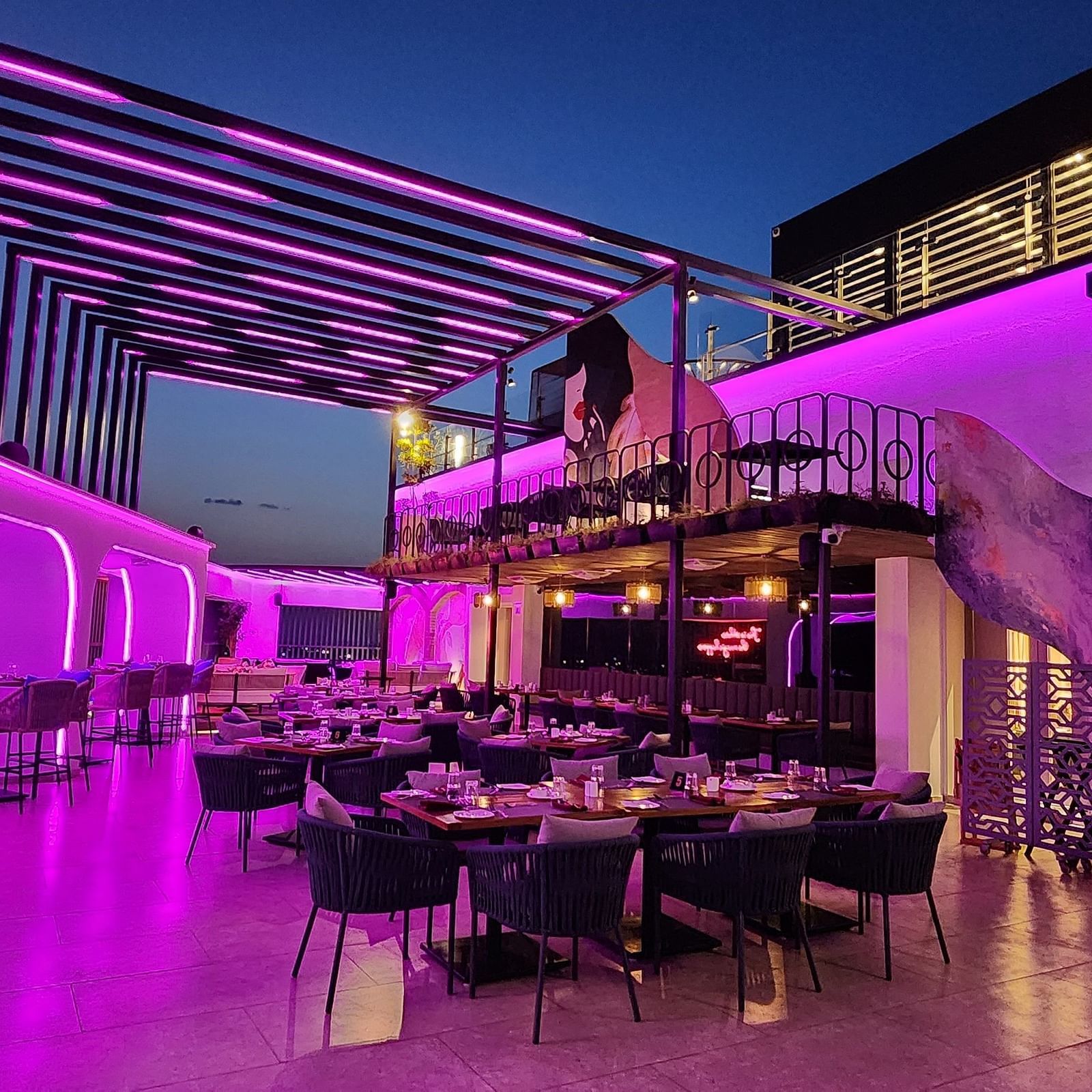wide angle shot of the rooftop dining area at Lords Inn Rajkot with variously arranged dining area on the floor, a balcony with seating area, and  a dimly lit ambience