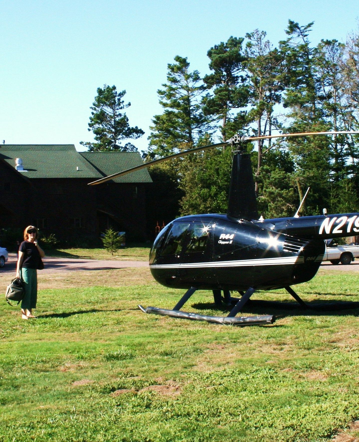 A woman dressed in black walking from a barn type building towards a helicopter ready to take off - Brewery Gulch Inn & Spa