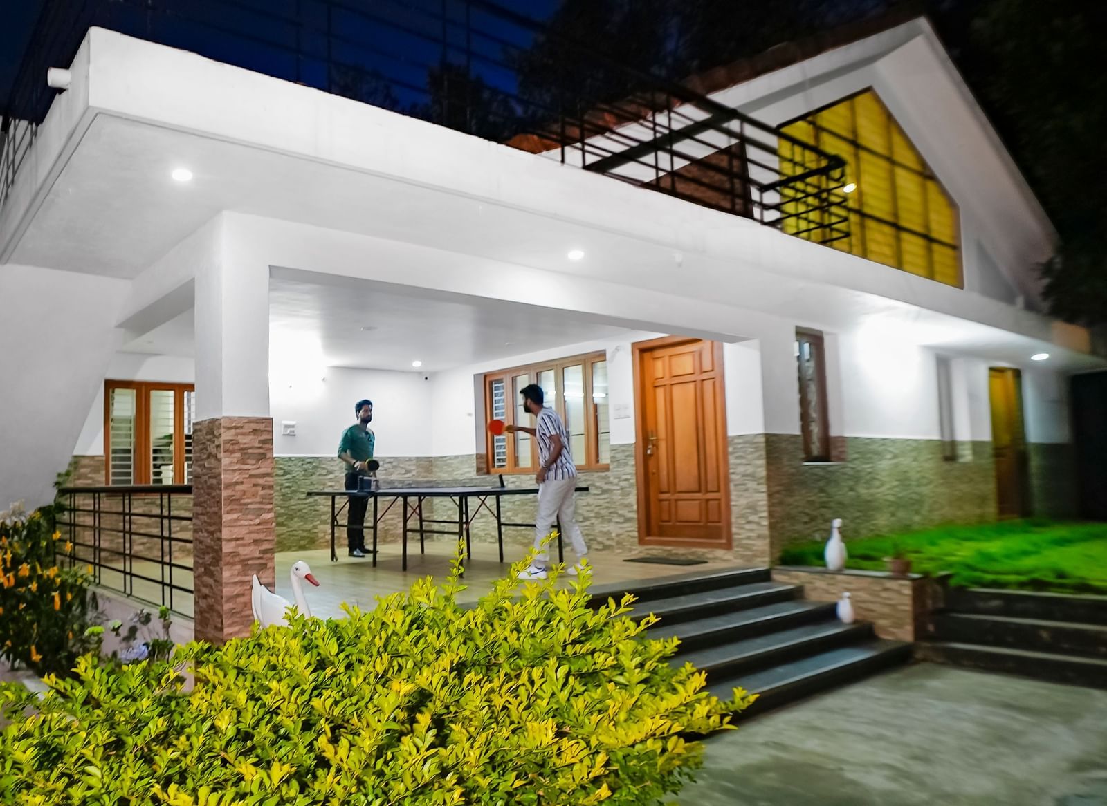 Facade view of WOW Bungalow, Yercaud, with two people playing table tennis on the porch.