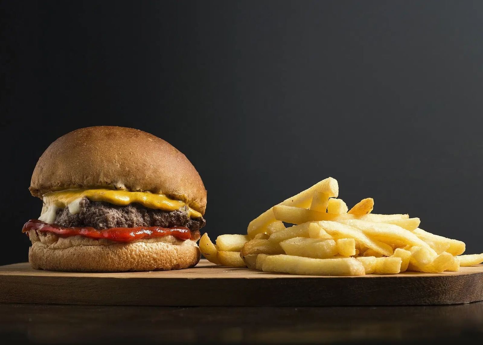 A classic cheeseburger served with a side of golden french fries on a dark background | Altamont Court, Jamaica