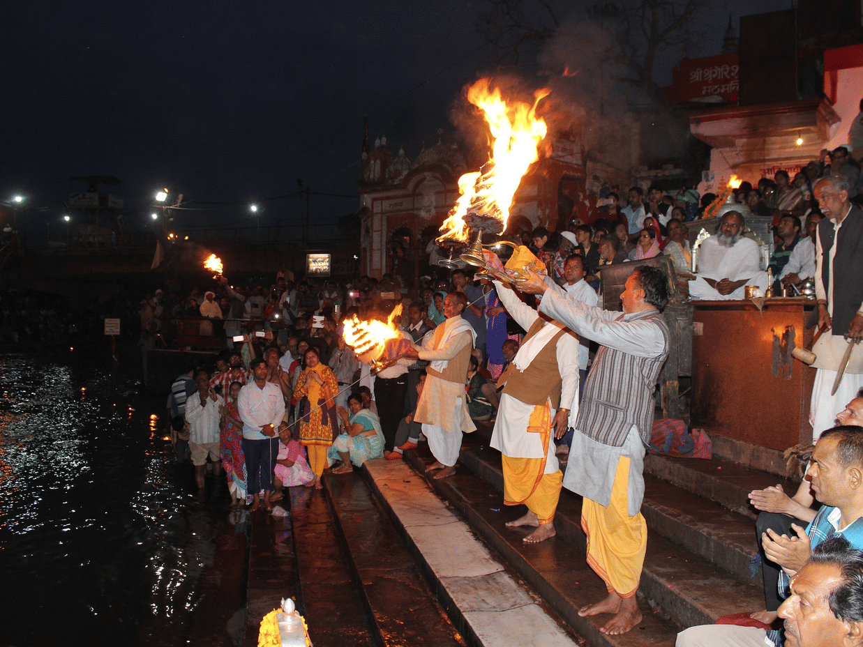 People performing Ganga aarti on the banks of a river with diyas.