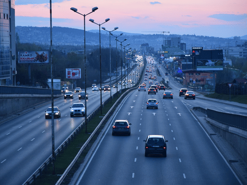 Aerial view of a city highway with vehicles in motion under an orange evening sky.