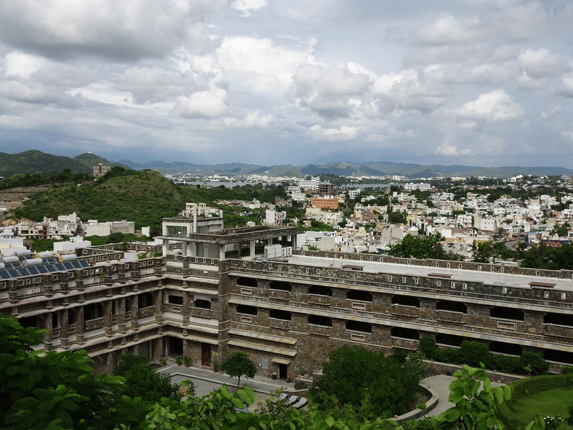 High-angle view of a large, modern stone building complex nestled amongst green hills and a sprawling city.