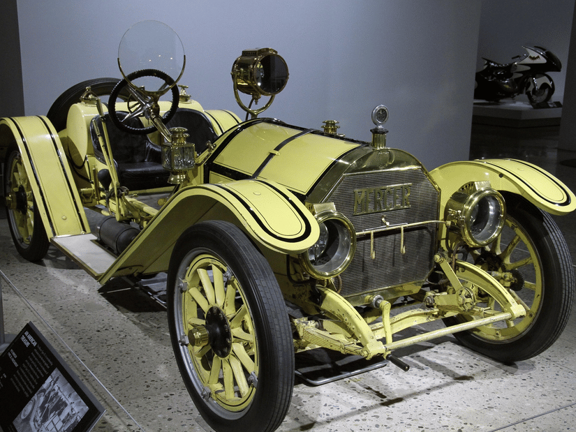 A classic yellow vintage racing car with large wooden-spoke wheels on display in a museum.