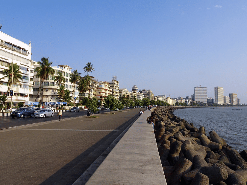 A wide promenade with people walking along a seafront lined with buildings and palm trees.